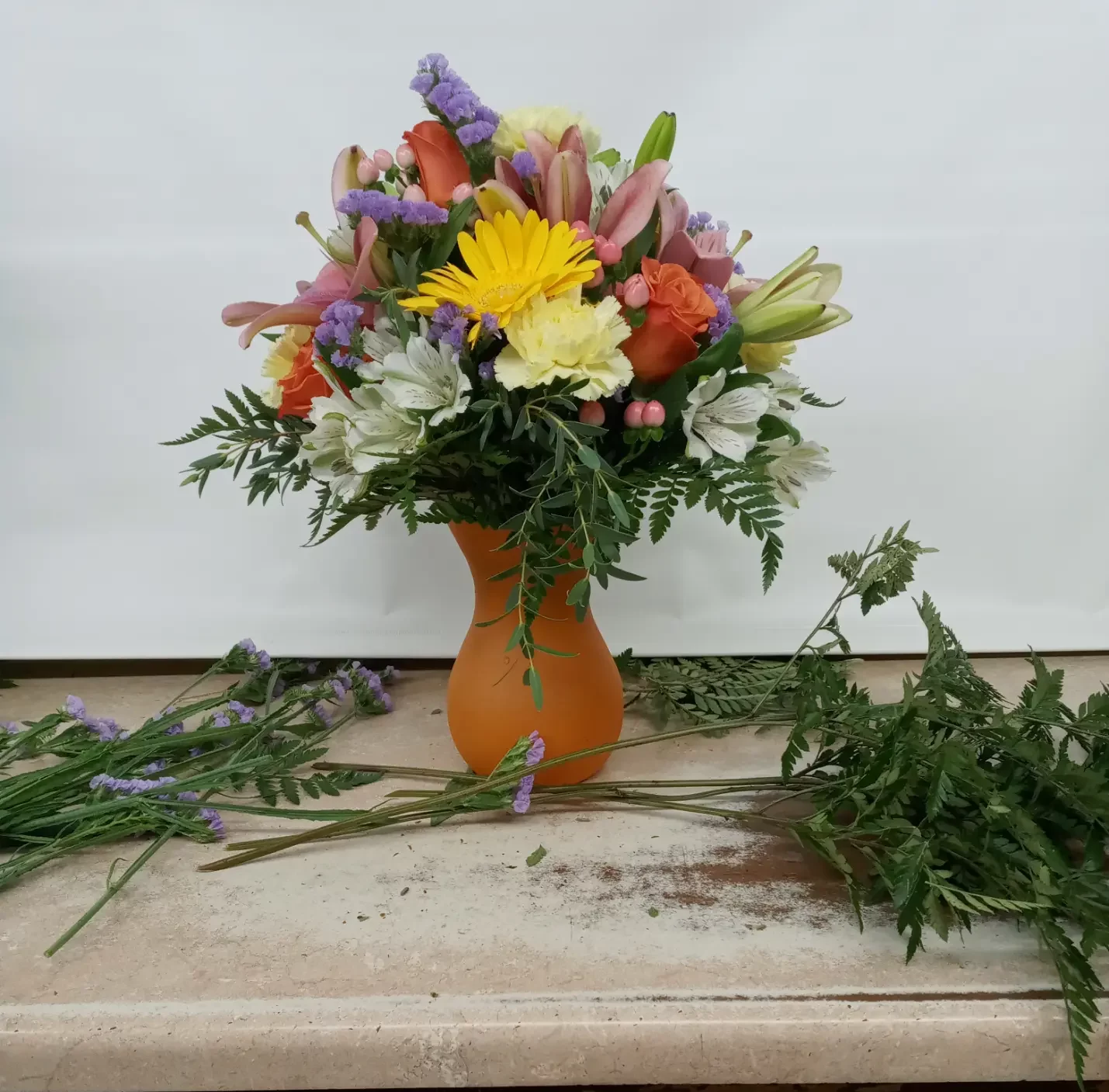Female florist in white shirt and apron arranging orange and white flowers for floral design