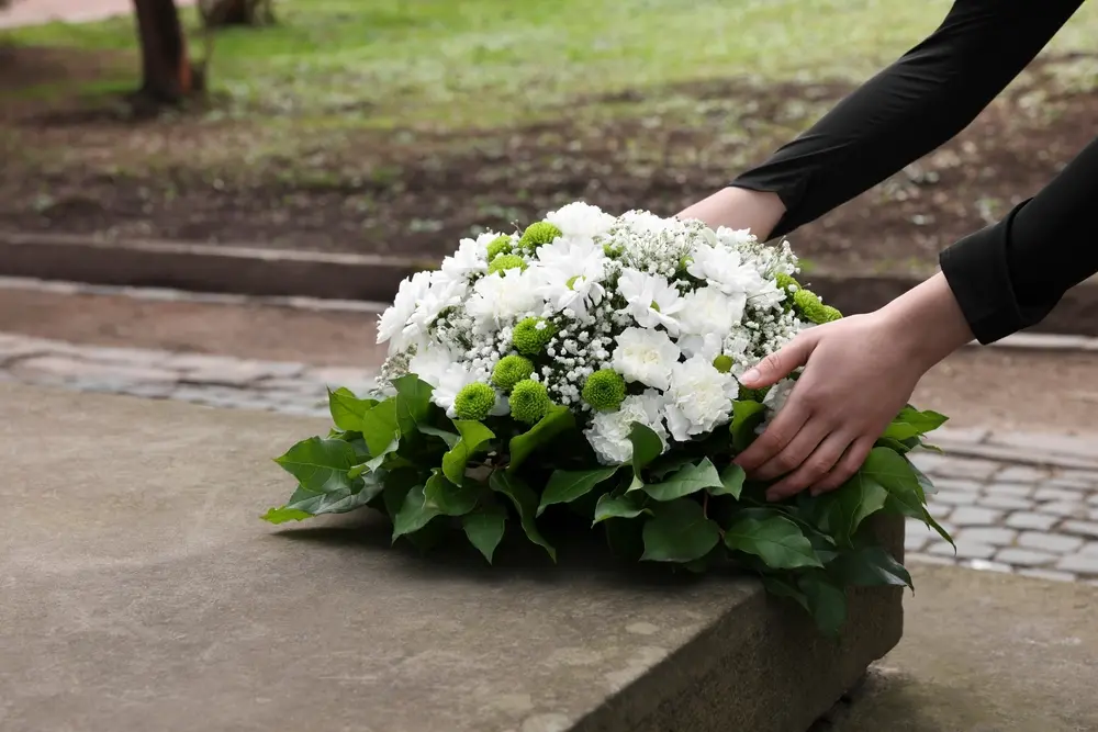 Person placing a white sympathy flower arrangement at a stone memorial